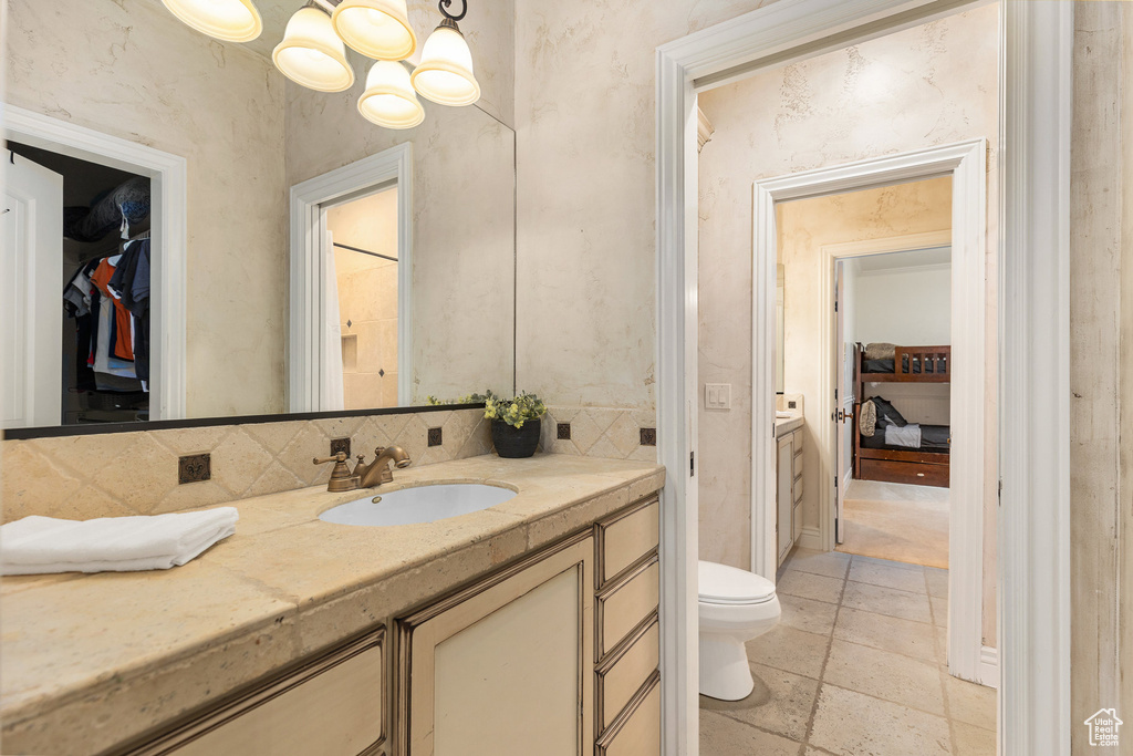 Bathroom with vanity, backsplash, a chandelier, a walk in closet, and stone tile floors