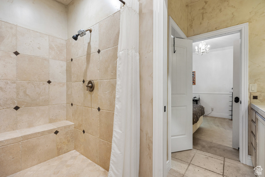 Bathroom with tiled shower, vanity, a chandelier, and a wainscoted wall