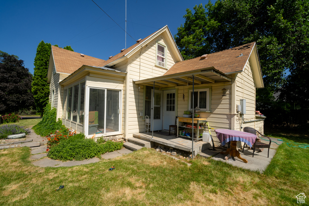 Rear view of house with a shingled roof, a lawn, and a patio area