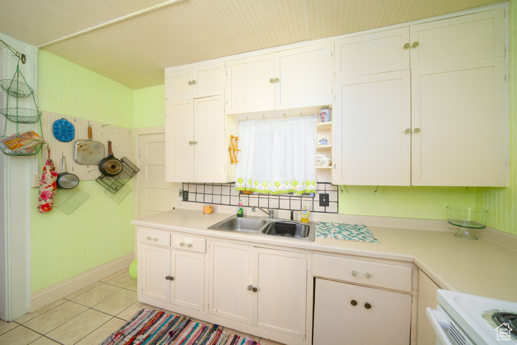 Kitchen with light countertops, light tile patterned flooring, range, white cabinets, and open shelves
