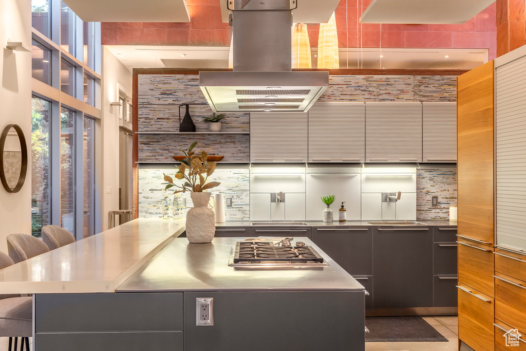 Kitchen with range hood, modern cabinets, tasteful backsplash, and stainless steel counters