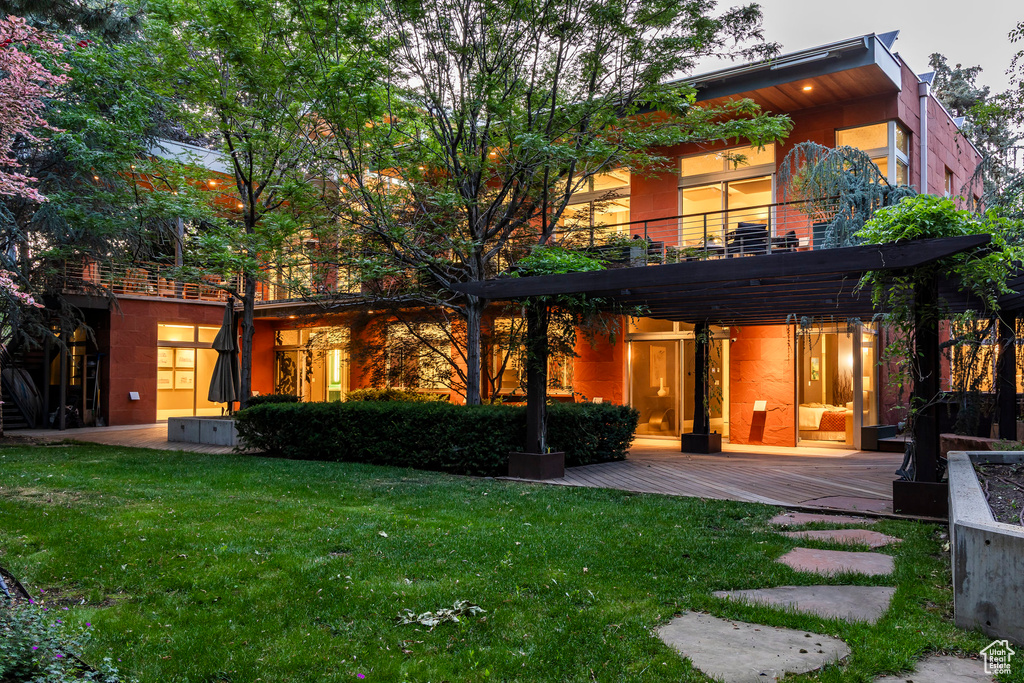 Back of property with a balcony, a lawn, and a deck