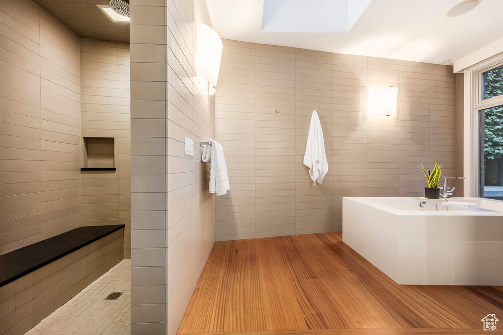 Full bath featuring wood finished floors, tile walls, a skylight, and walk in shower