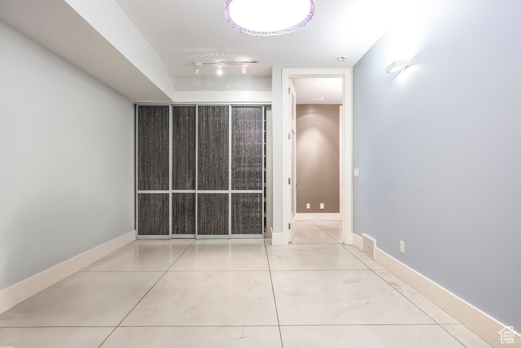 Tiled empty room featuring rail lighting and baseboards
