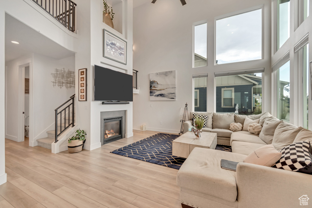 Living room with a towering ceiling, a glass covered fireplace, light wood-type flooring, stairway, and ceiling fan