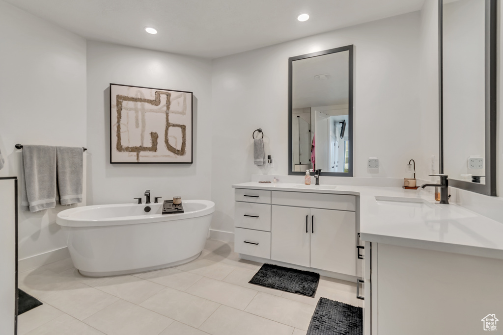 Full bath with double vanity, a freestanding bath, tile patterned flooring, and recessed lighting