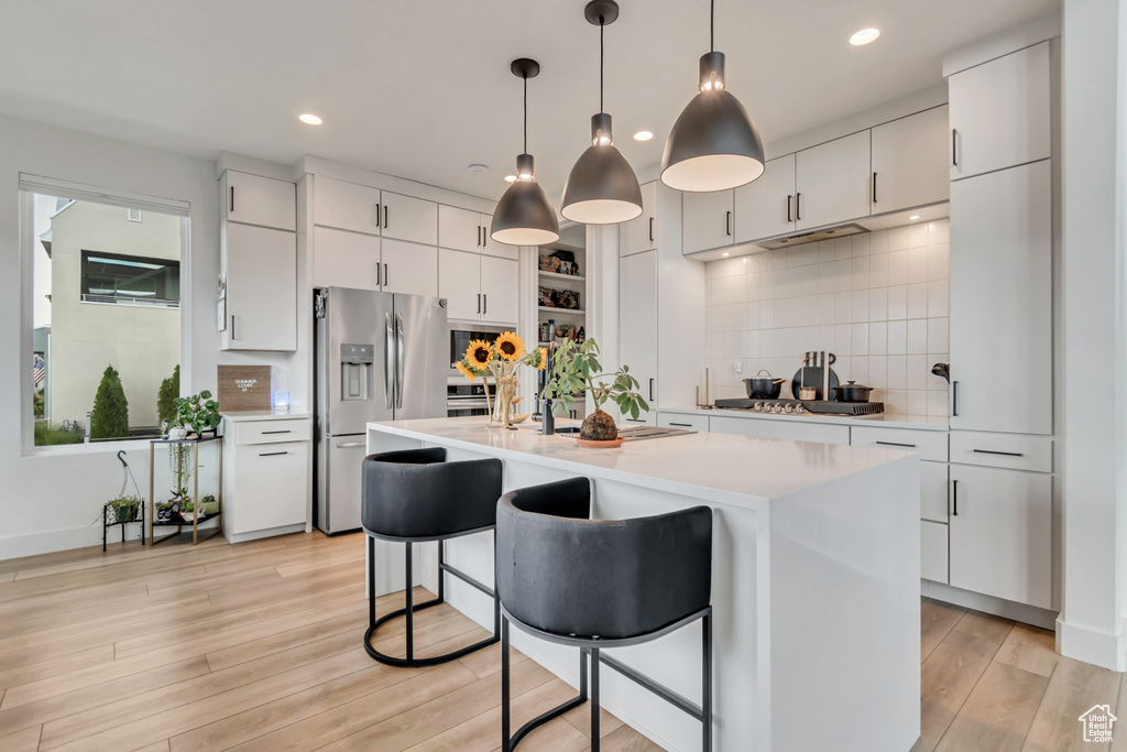 Kitchen with stainless steel appliances, light countertops, tasteful backsplash, white cabinetry, and a breakfast bar area