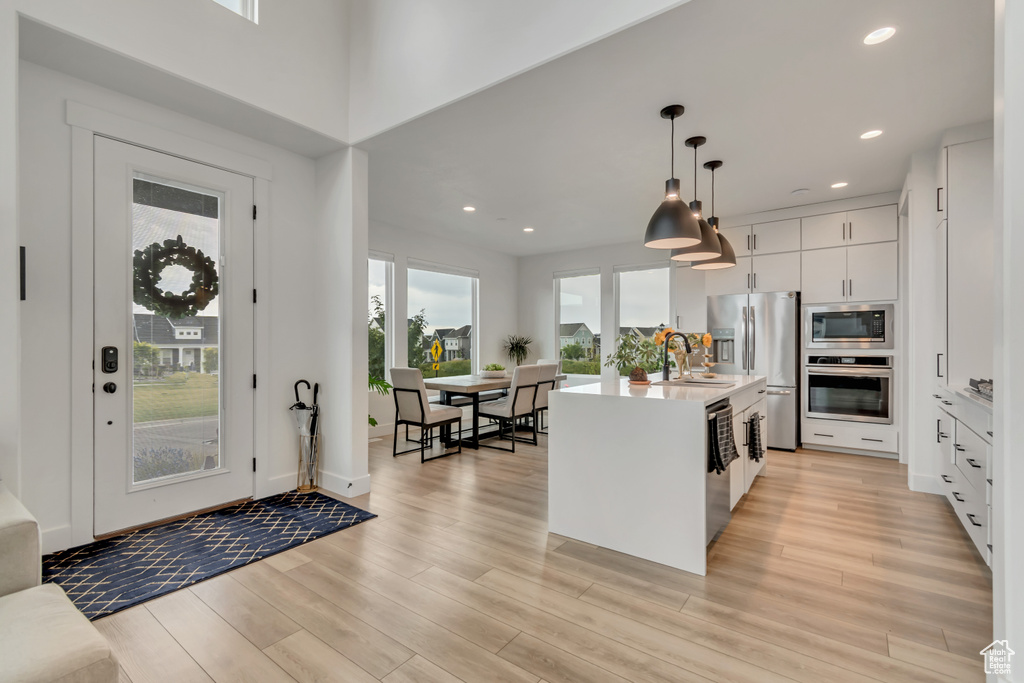 Kitchen with appliances with stainless steel finishes, light wood-type flooring, light countertops, decorative light fixtures, and white cabinets