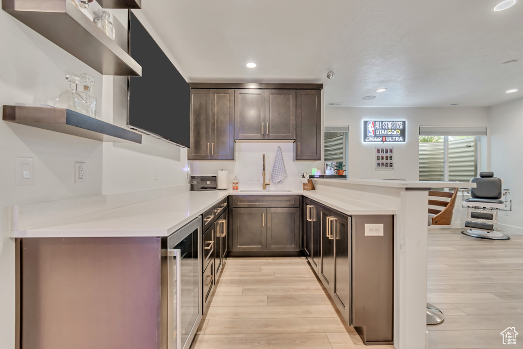 Kitchen featuring open shelves, a peninsula, wine cooler, light wood-style floors, and recessed lighting