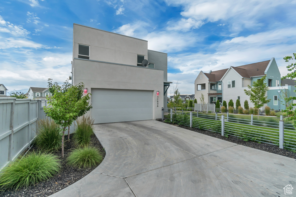 Modern home with a garage, a residential view, concrete driveway, and stucco siding