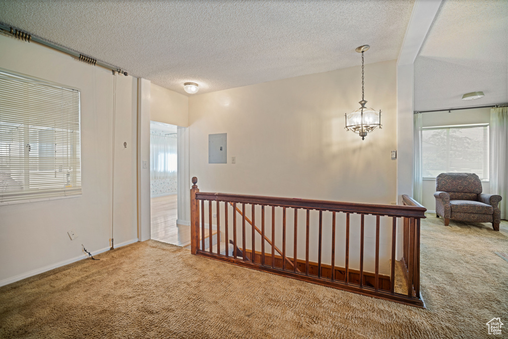 Corridor featuring carpet floors, electric panel, an upstairs landing, a chandelier, and a textured ceiling