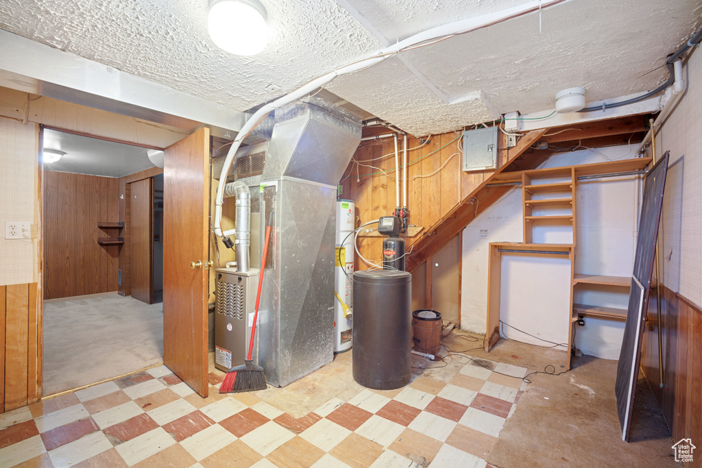 Below grade area with tile patterned floors, a water softener, wood walls, heating unit, and a textured ceiling
