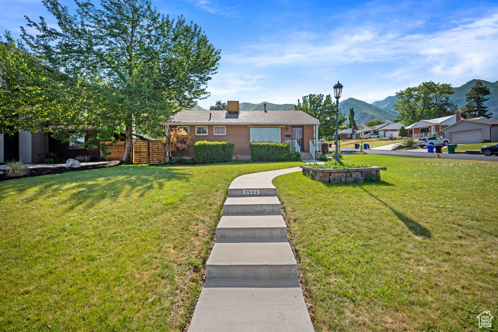 Ranch-style house with a front lawn, a mountain view, brick siding, and a chimney