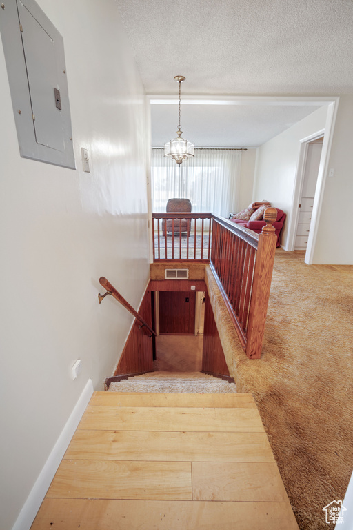 Stairs featuring electric panel, a textured ceiling, and a chandelier