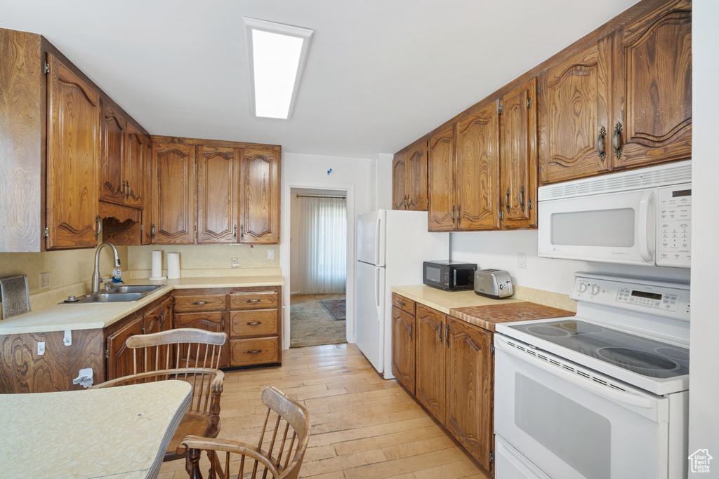 Kitchen featuring white appliances, light wood-style flooring, brown cabinetry, and light countertops