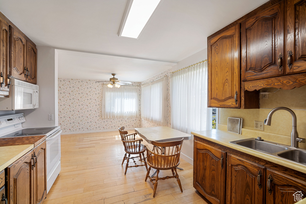 Kitchen with white appliances, healthy amount of natural light, wallpapered walls, light wood-style floors, and ceiling fan