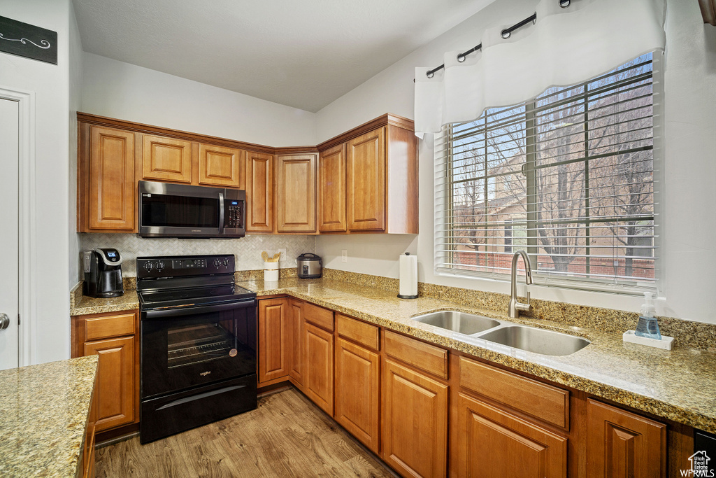 Kitchen featuring black range with electric stovetop, stainless steel microwave, light wood-type flooring, light stone countertops, and plenty of natural light