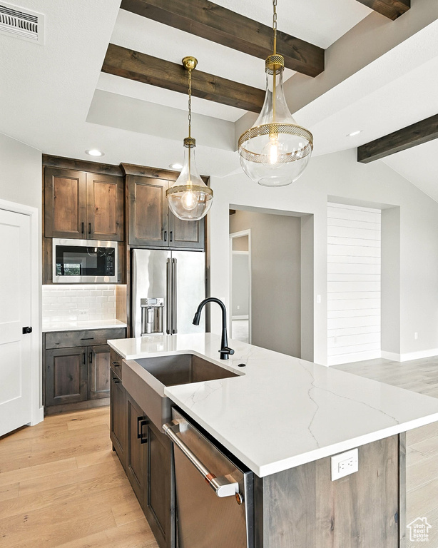 Kitchen with stainless steel appliances, a kitchen island with sink, light wood-type flooring, backsplash, and beamed ceiling