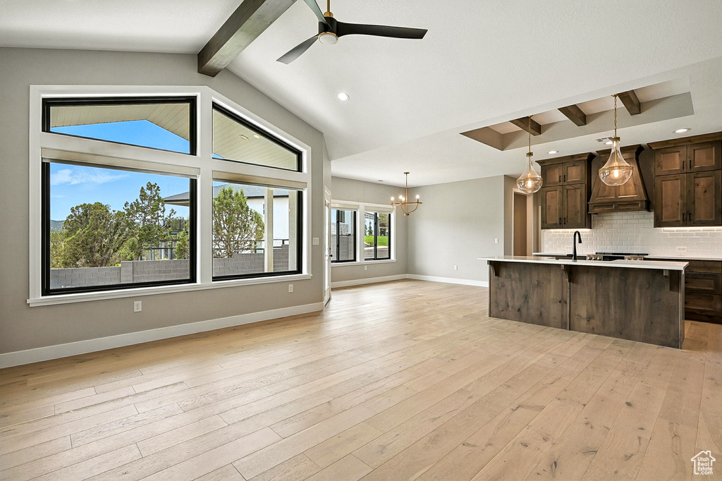 Kitchen with custom range hood, open floor plan, dark brown cabinets, light countertops, and backsplash