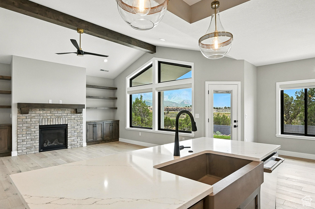 Kitchen with light wood finished floors, light stone counters, open floor plan, a fireplace, and a ceiling fan