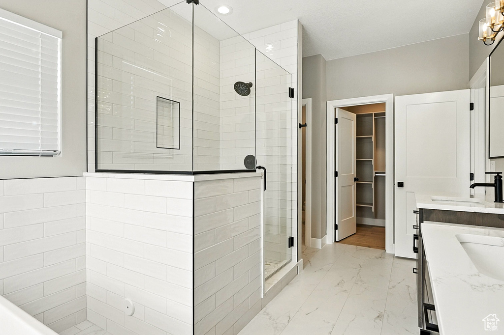 Bathroom featuring marble look tile flooring, a stall shower, double vanity, a spacious closet, and recessed lighting