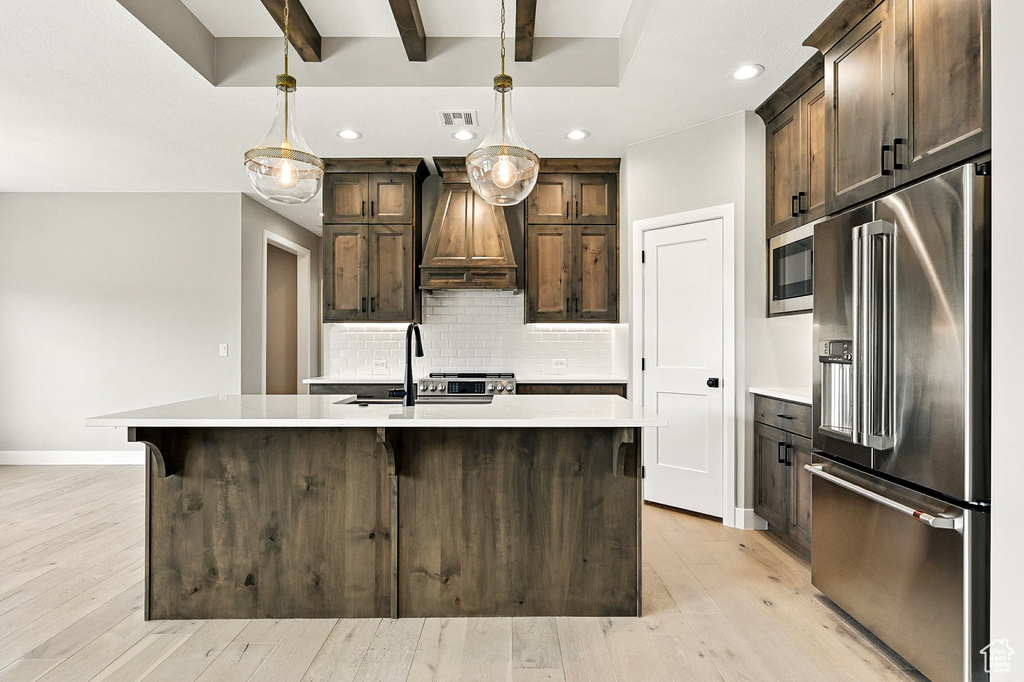 Kitchen with stainless steel appliances, custom range hood, light countertops, light wood-style flooring, and recessed lighting