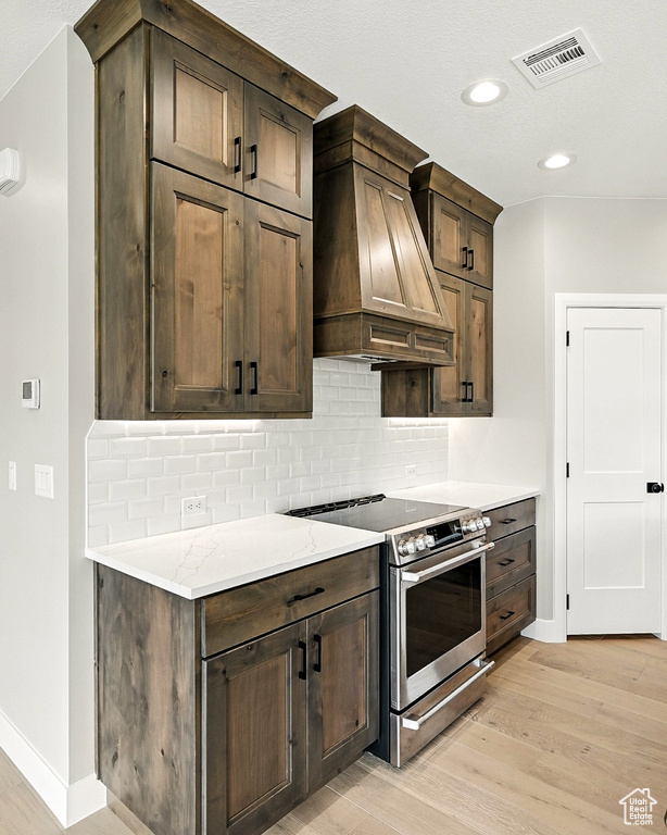 Kitchen featuring stainless steel electric stove, custom range hood, light wood finished floors, decorative backsplash, and recessed lighting