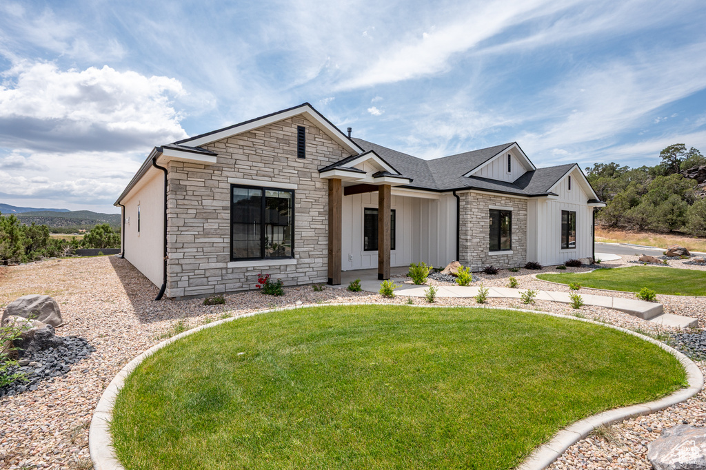 Modern inspired farmhouse featuring stone siding, board and batten siding, a front lawn, and a shingled roof