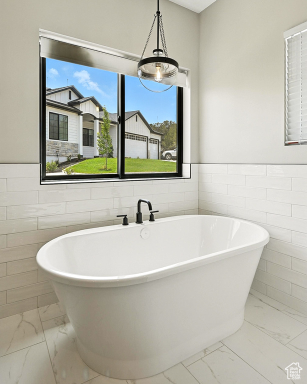 Bathroom with marble finish floors, tile walls, plenty of natural light, a freestanding bath, and a wainscoted wall