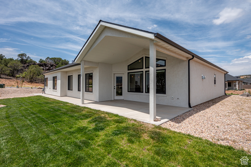 Rear view of property with stucco siding, a lawn, and a patio