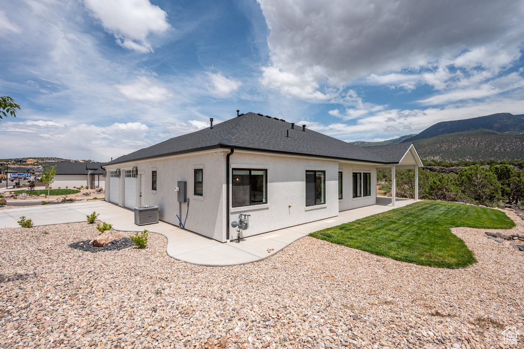 Back of house with roof with shingles, concrete driveway, stucco siding, a mountain view, and an attached garage