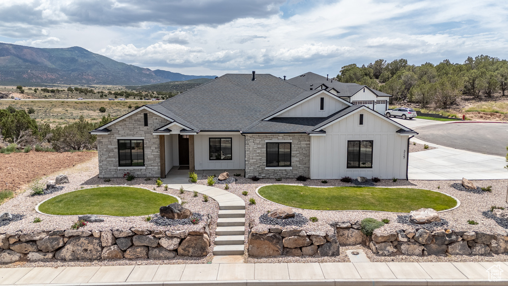 Modern farmhouse featuring board and batten siding, stone siding, roof with shingles, a front yard, and a mountain view