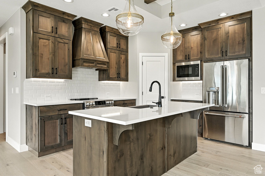 Kitchen featuring appliances with stainless steel finishes, custom exhaust hood, light wood-style flooring, light countertops, and recessed lighting