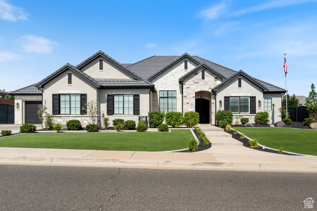 French country style house with stone siding, stucco siding, a front lawn, and a garage