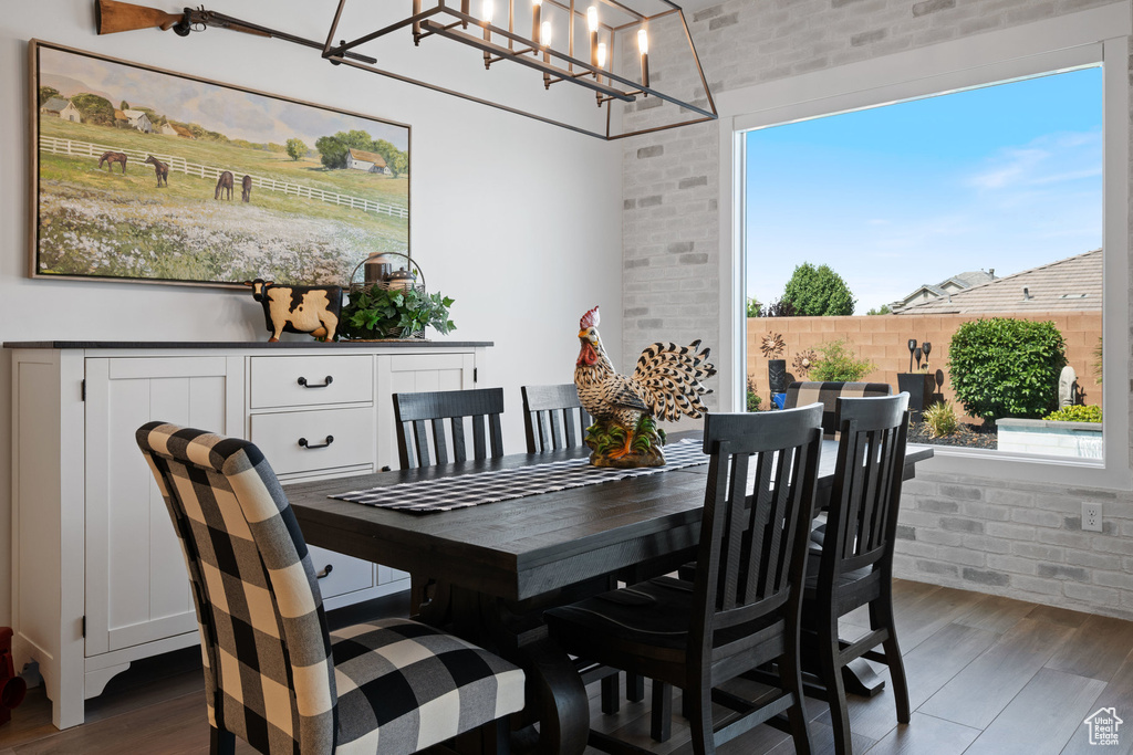 Dining area with wood finished floors, brick wall, a chandelier, and healthy amount of natural light