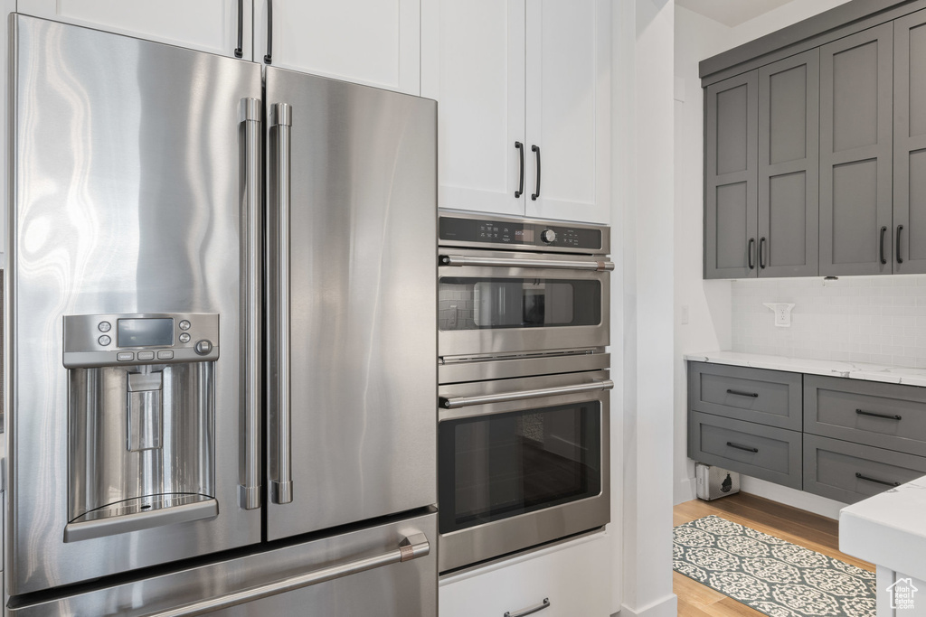 Kitchen with stainless steel appliances, gray cabinetry, light wood-type flooring, and light stone counters