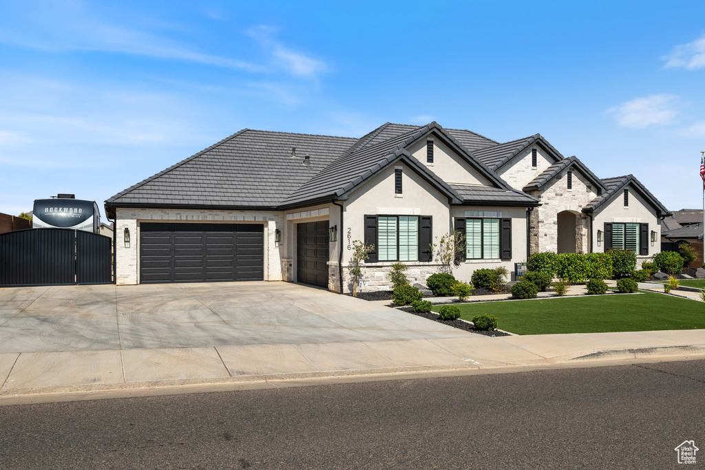 French country home with stone siding, a garage, a gate, driveway, and stucco siding