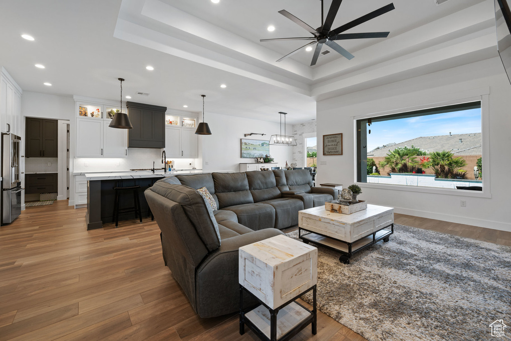 Living room with ceiling fan, recessed lighting, a raised ceiling, wood finished floors, and a chandelier