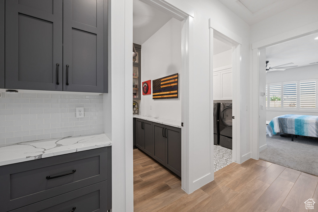 Bar with light wood finished floors, decorative backsplash, ceiling fan, and washer / dryer