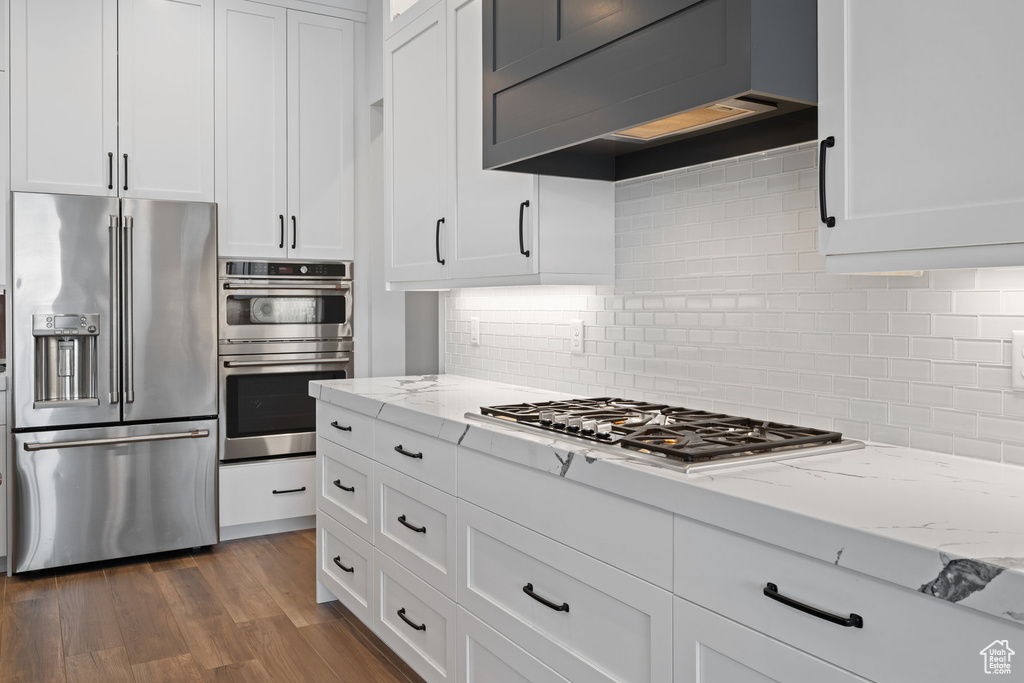 Kitchen featuring appliances with stainless steel finishes, white cabinetry, light stone countertops, and dark wood finished floors