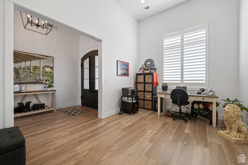 Office area with light wood-style flooring, a chandelier, and a towering ceiling