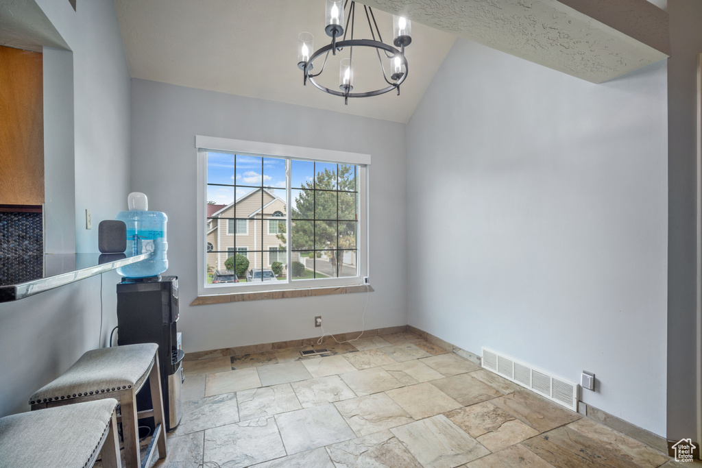 Unfurnished dining area featuring stone tile floors, a chandelier, and lofted ceiling