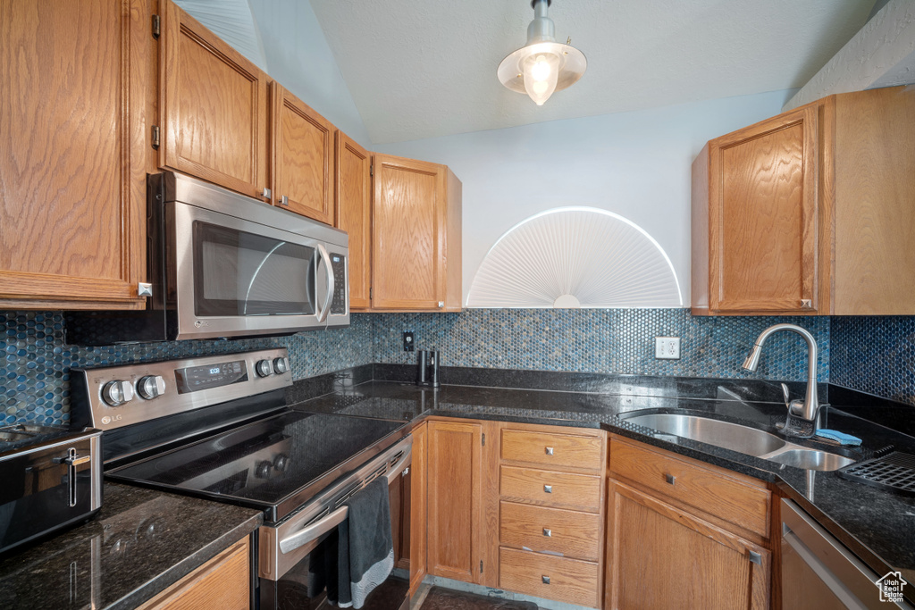 Kitchen featuring appliances with stainless steel finishes, dark stone countertops, backsplash, lofted ceiling, and brown cabinetry