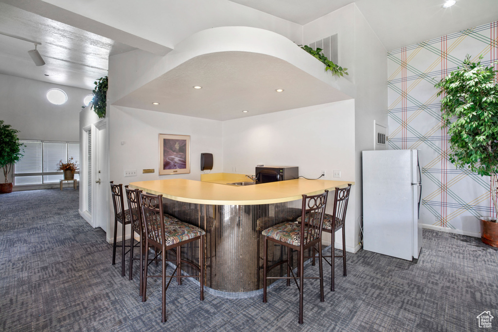 Bar area featuring freestanding refrigerator, dark carpet, wallpapered walls, black microwave, and recessed lighting