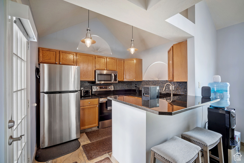 Kitchen with appliances with stainless steel finishes, a peninsula, backsplash, lofted ceiling, and hanging light fixtures