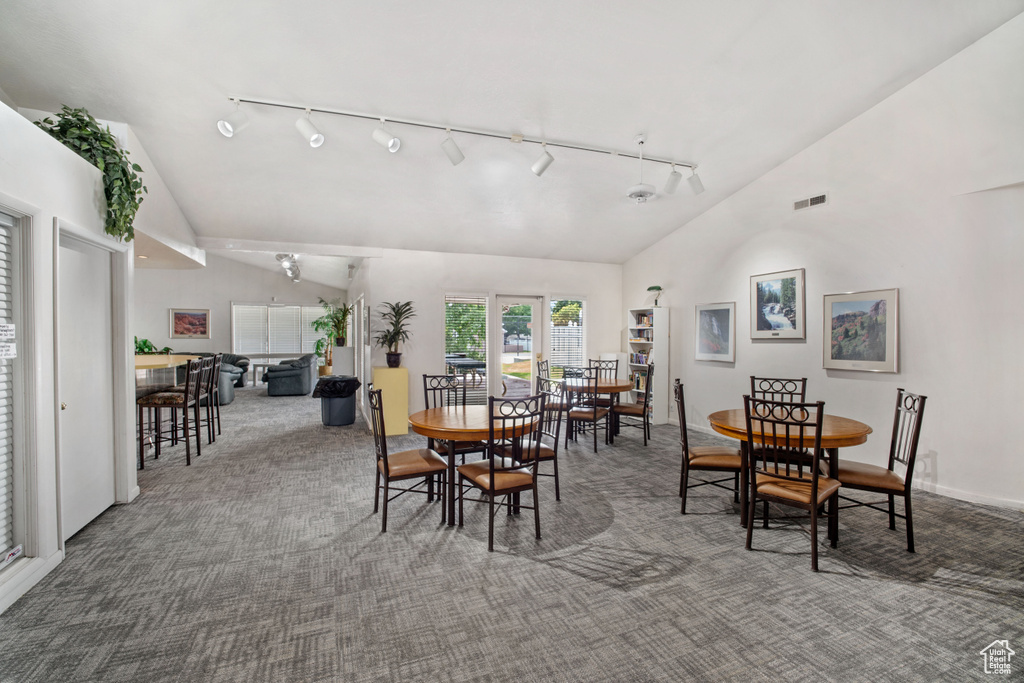 Dining space with rail lighting, carpet floors, and high vaulted ceiling
