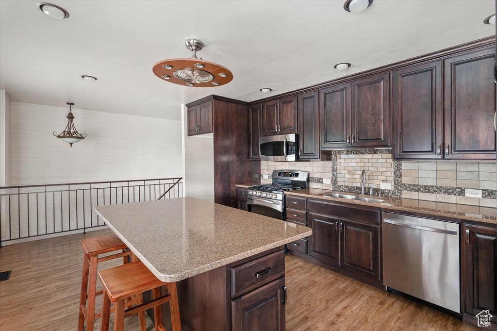 Kitchen with stainless steel appliances, dark brown cabinets, light wood-style floors, and tasteful backsplash