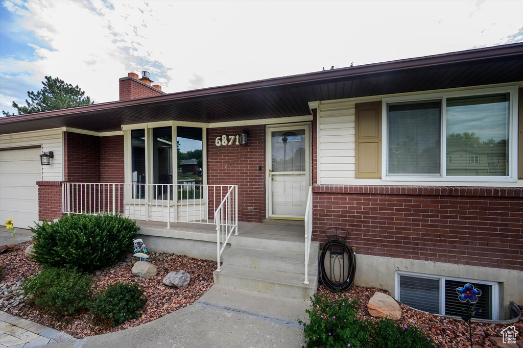 Entrance to property with a porch, brick siding, an attached garage, and a chimney