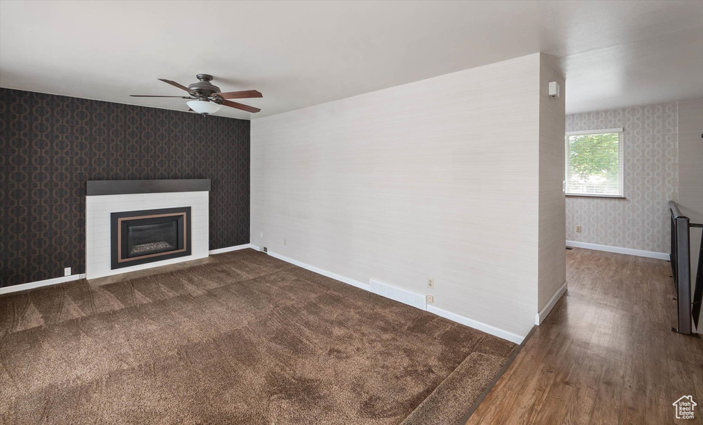 Unfurnished living room featuring wallpapered walls, ceiling fan, a glass covered fireplace, wood finished floors, and an accent wall