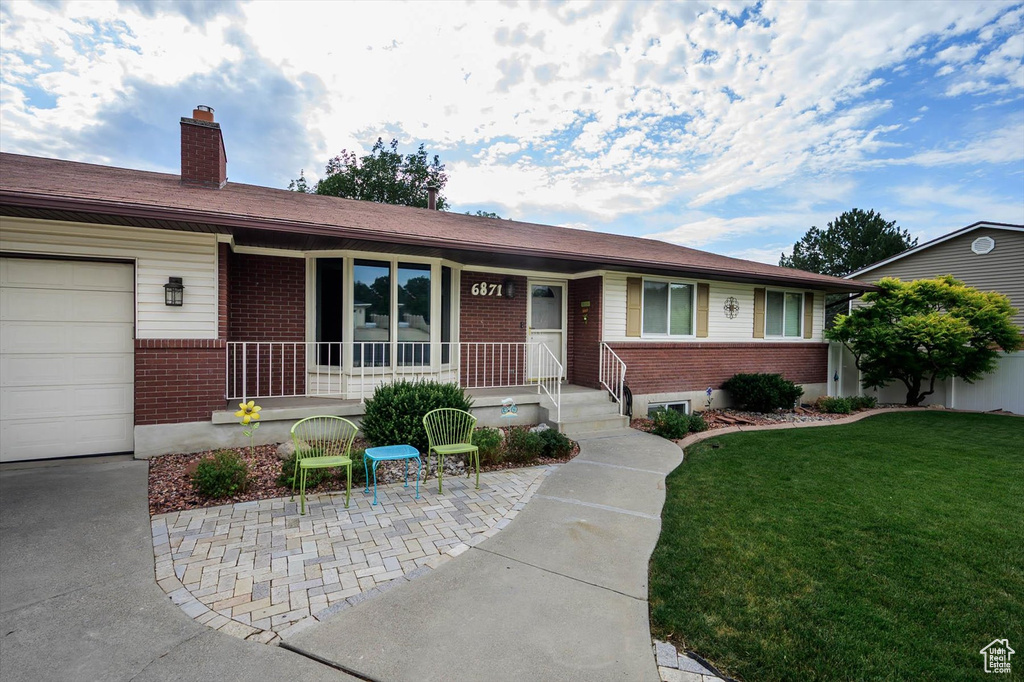 Single story home featuring brick siding, a front yard, a chimney, a porch, and an attached garage